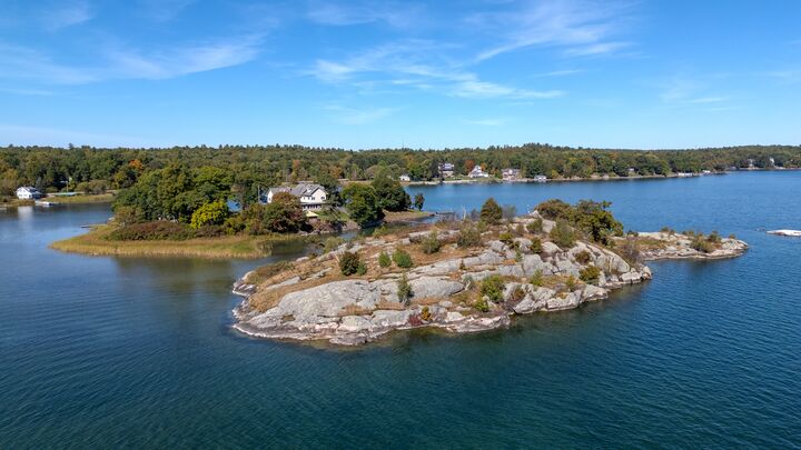 Wooded island in a lake under a clear blue sky, seen from the air