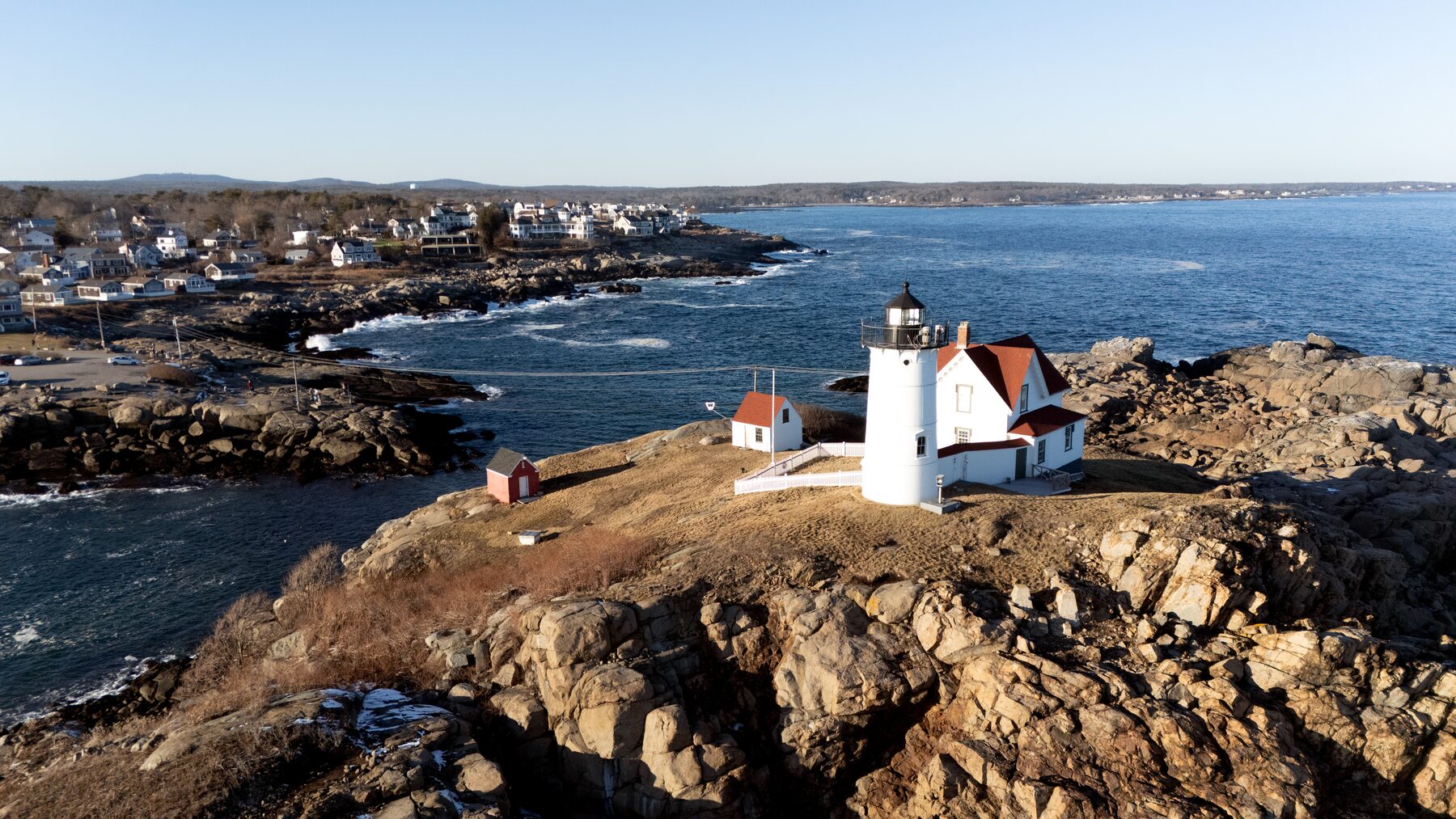 White lighthouse on a rocky point, with a village behind it