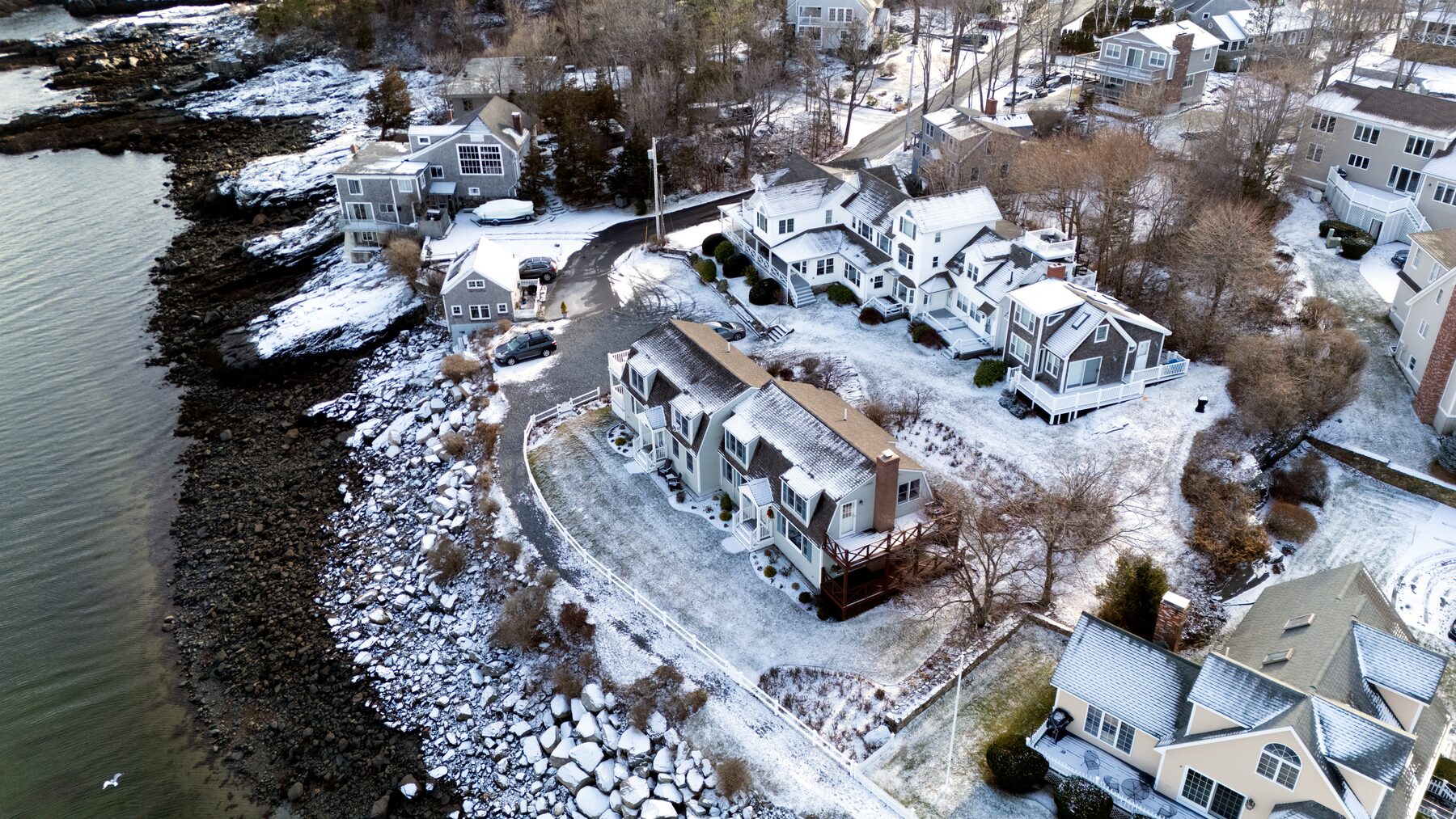 Snow-dusted houses along a rocky shoreline, from above