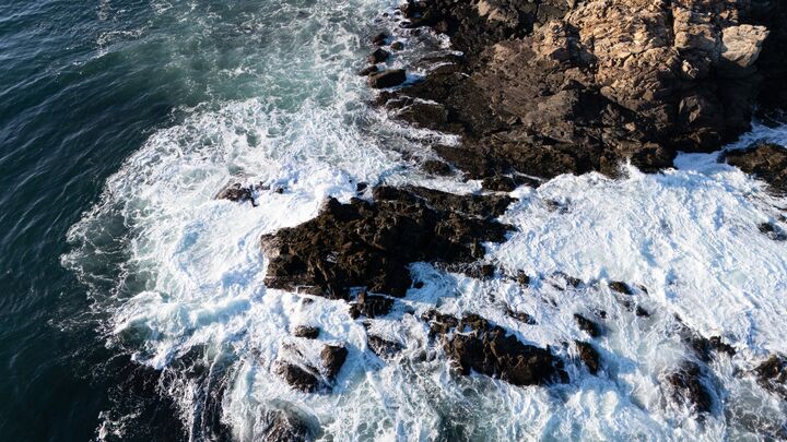 Waves breaking over dark rocks, seen from directly above