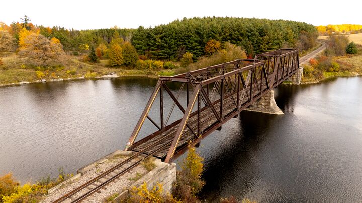 Steel truss rail bridge crossing a river at the edge of a forest