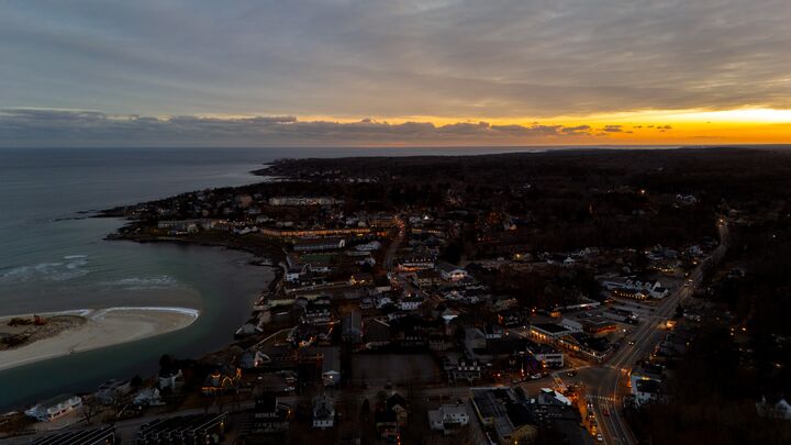 Coastal town at dusk with streetlights coming on and sunset on the horizon