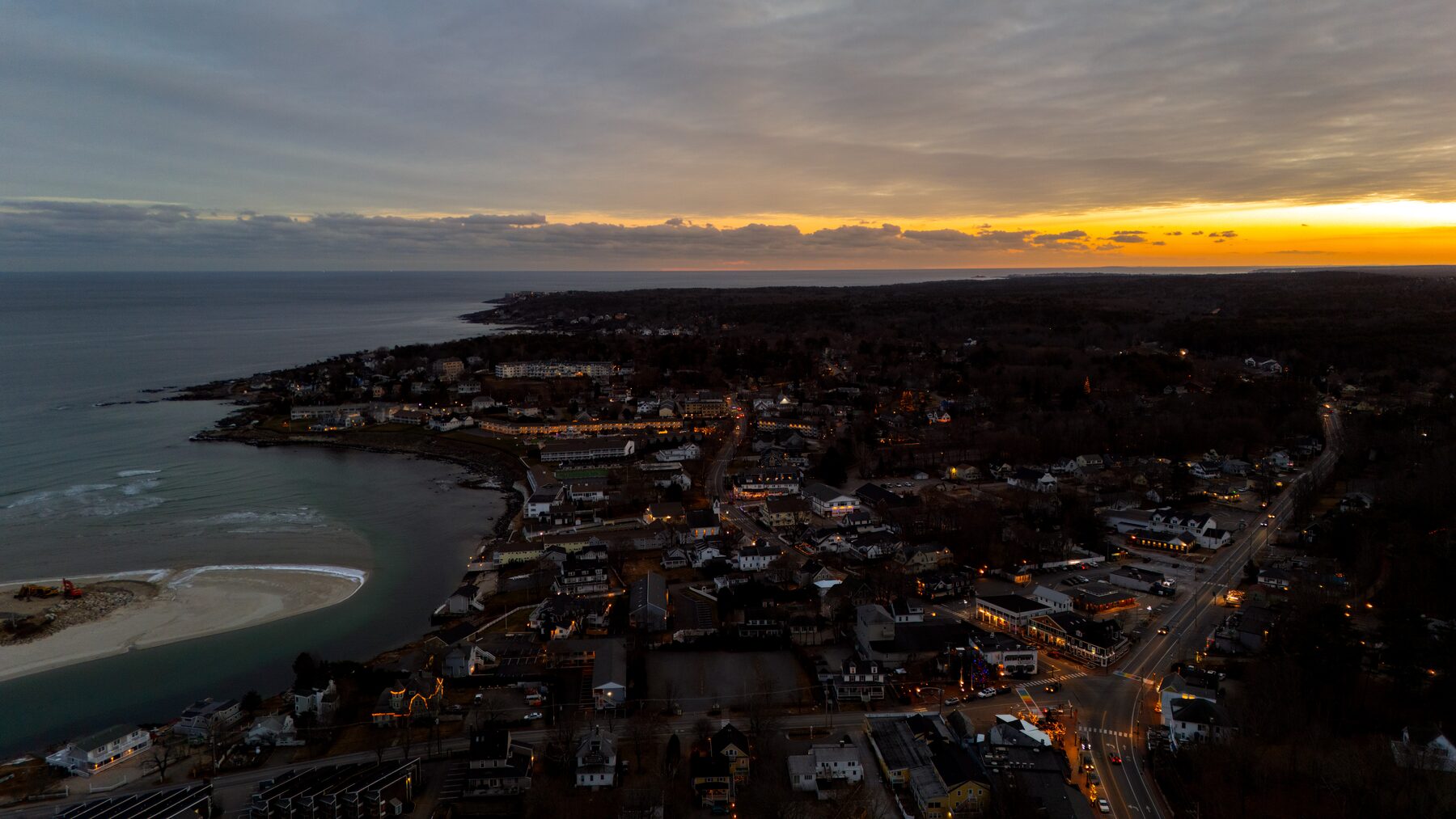 Coastal town at dusk with streetlights coming on and sunset on the horizon