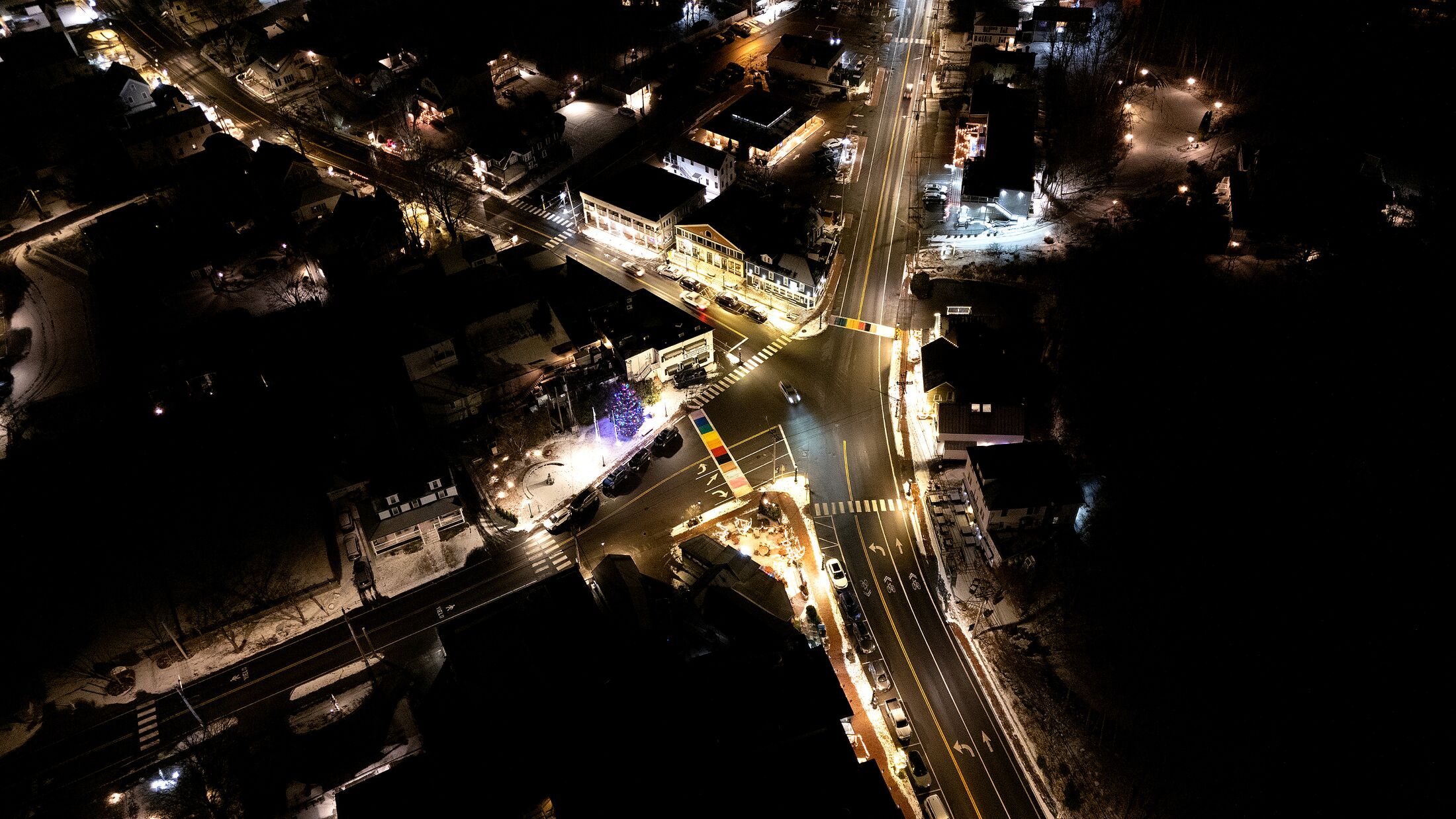 Small town intersection at night from the air, streets lit and a decorated tree at the corner